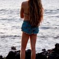 A young woman with long wavy hair looks out over lake from a rocky shore